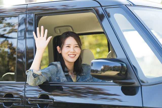 車から笑顔で手を振る女性